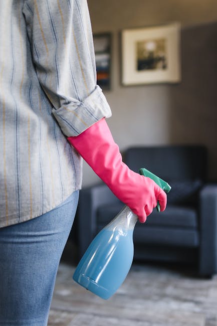 Three professional cleaners from Carpet Cleaners N5 stand in a modern living room during surface cleaning and sanitisation. The room features light-colored wooden flooring, a dark fabric sofa with cus