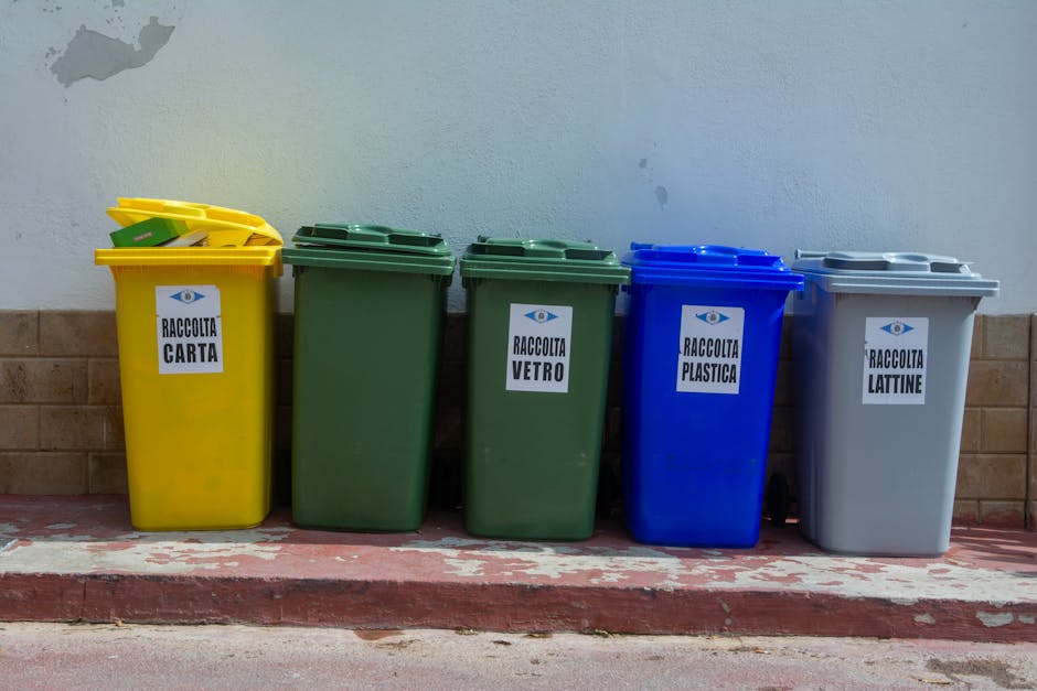 A white commercial van parked outside a building with large glass windows, partially visible on the left. In front of the van, there are three blue garbage bags filled with waste placed on the pavemen